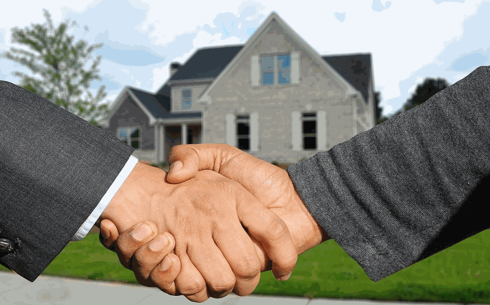 Two people shaking hands in front of a blurred house exterior with green lawn and blue sky